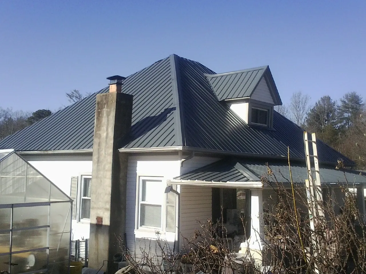 Dark blue standing seam metal roof on a white farmhouse with dormer — Slate & Tile Roof Repair by Roofing Brothers in Hempstead