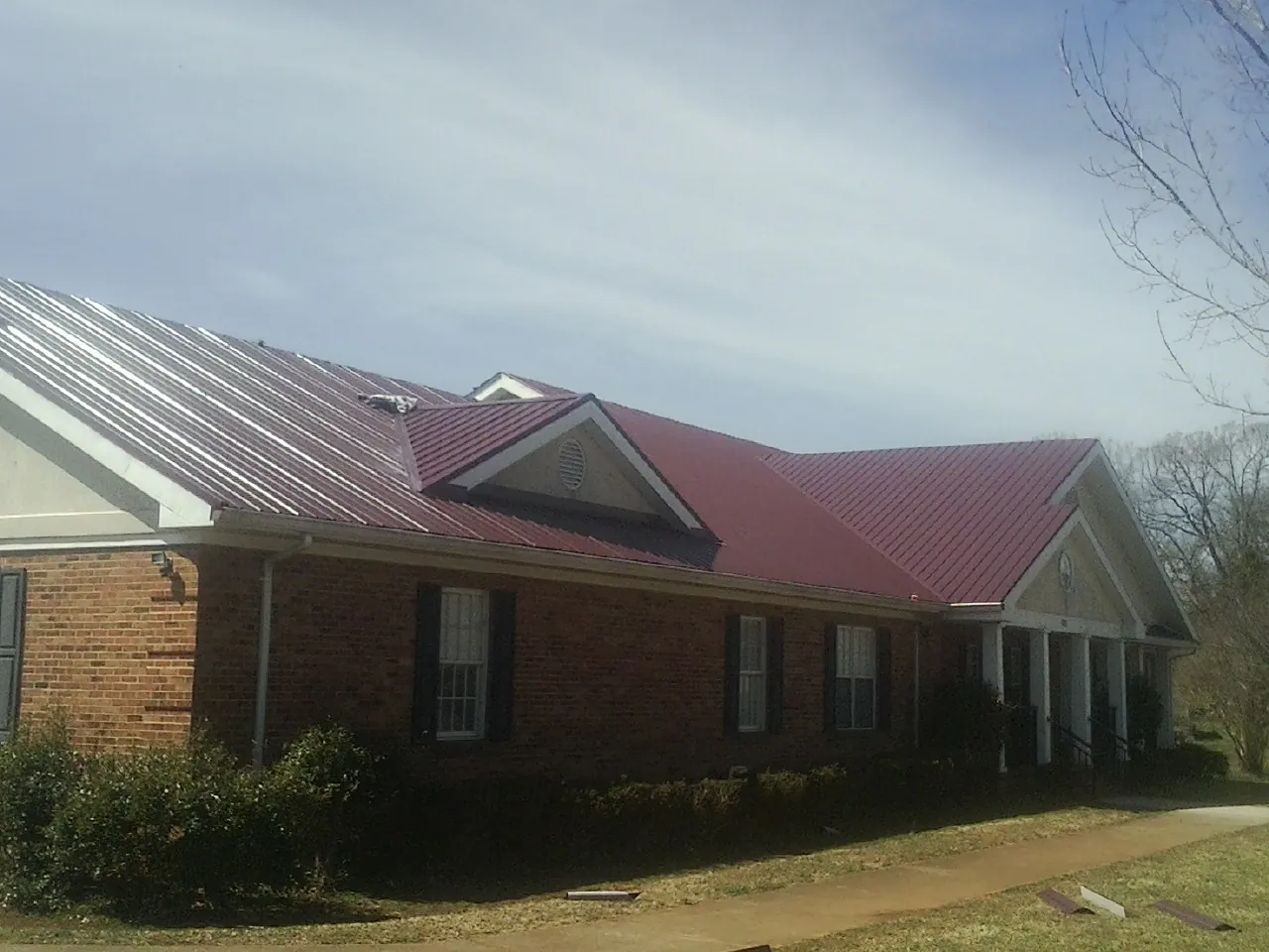 Red metal roof with gabled entries on a long brick building, from a Hail Damage Roof Repair job in Hempstead