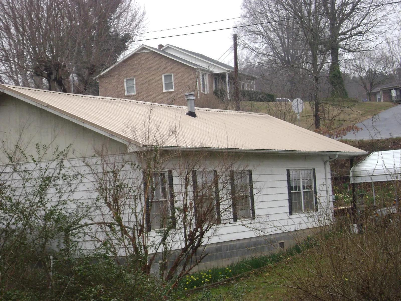 Tan metal roof on a white sided house set into a hillside — Commercial Roofing by Roofing Brothers in Hempstead